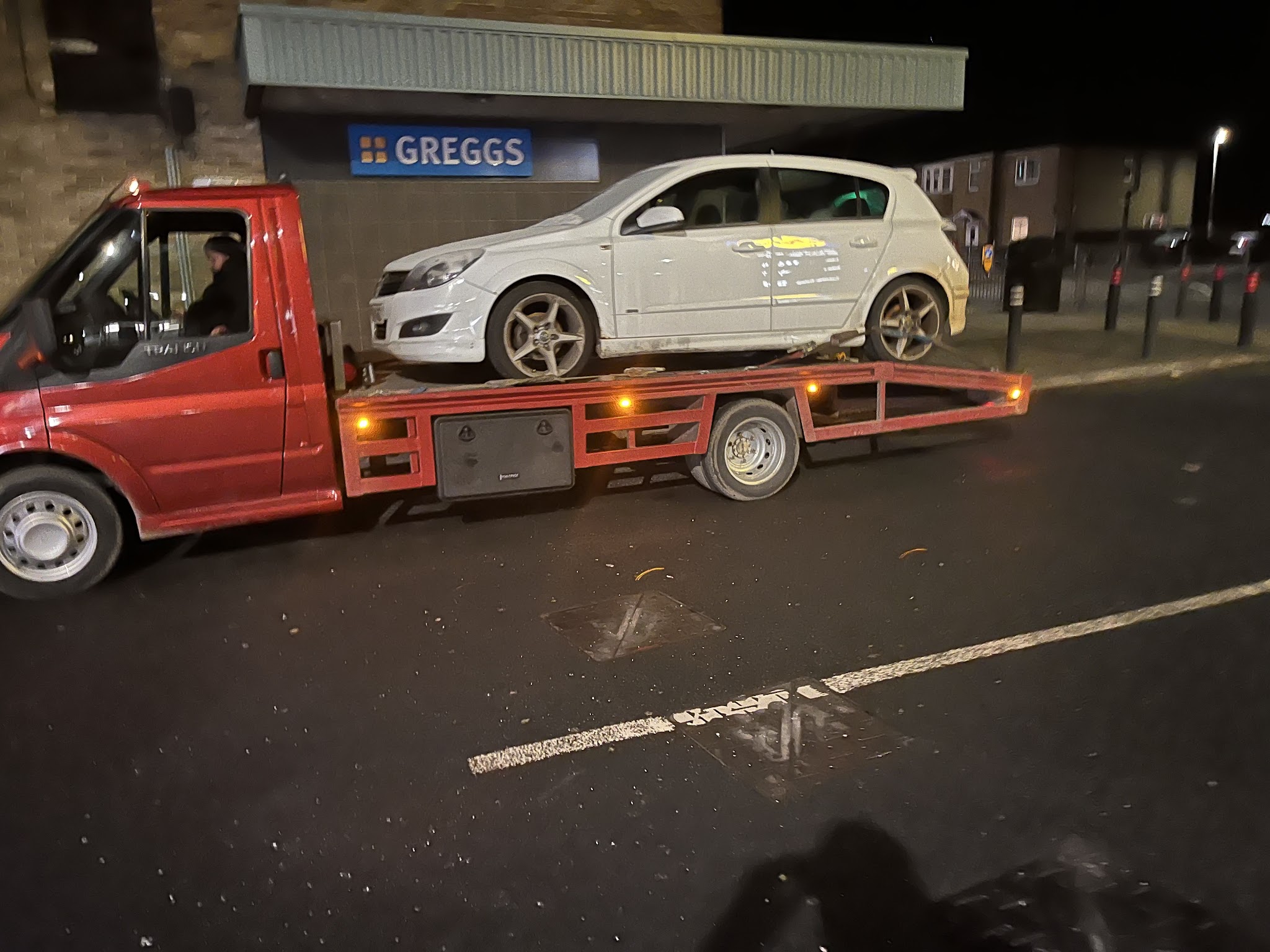 Recovery truck carrying a white hatchback at night
