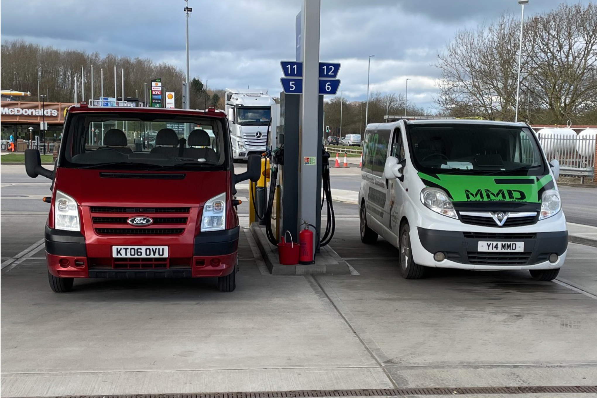 The red recovery truck parked next to the white MMD van at a fuel station